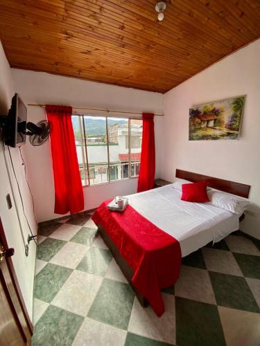 a bedroom with a bed with red sheets and a window at Hotel Policarpa in Guaduas