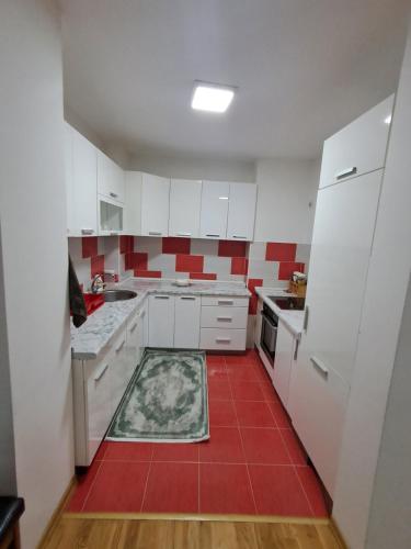 a kitchen with white cabinets and a red tile floor at Stan u centru grada Rozaje in Rožaje