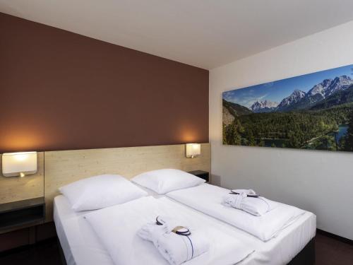 a bedroom with a large white bed with a painting on the wall at Sunday Hotel Garmisch Partenkirchen in Garmisch-Partenkirchen