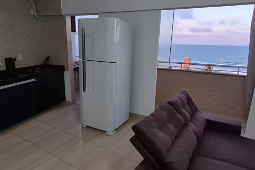a kitchen with a refrigerator and a couch in front of a window at Apartamento brisa do oceano in Natal