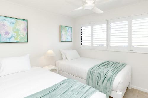 a white bedroom with two beds and a window at Beachfront Canvas - Ocean Views Pool Gym in Mudjimba