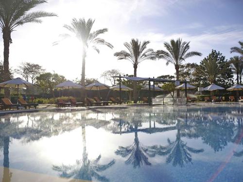 a large swimming pool with palm trees and umbrellas at Novotel Cairo 6th Of October in 6th Of October