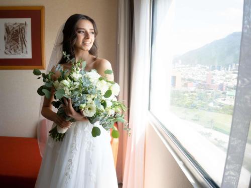 a bride holding a bouquet in front of a window at Novotel Monterrey Valle in Monterrey