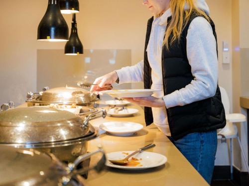 Una mujer parada en una cocina preparando comida. en Mercure Canberra, en Canberra