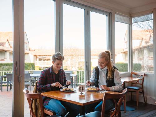 Un hombre y una mujer sentados en una mesa comiendo comida en Mercure Canberra, en Canberra