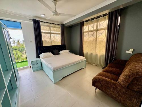 a bedroom with a bed and a couch and windows at IVORY Home 2 in Dar es Salaam