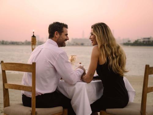 un homme et une femme assis à une table sur la plage dans l'établissement Sofitel Dubai The Palm Resort & Spa, à Dubaï