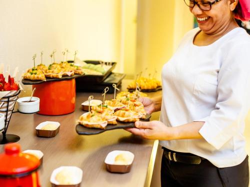 Eine Frau, die ein Tablett mit Essen auf der Theke hält. in der Unterkunft Novotel Porto Alegre Airport in Porto Alegre