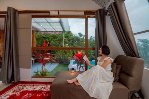 a woman sitting on a couch looking out a window at เดอะ ม้ง โฮมสเตย์ The Hmong Home Stay Chiangmai in Ban Tai