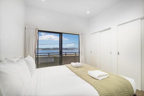 a white bedroom with a bed with two towels on it at Sea Views at 7 - Beachside Apartment in Whitianga