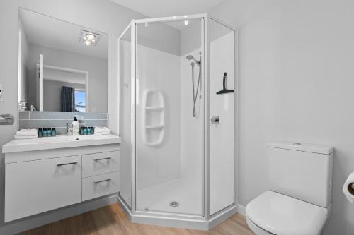 a white bathroom with a shower and a toilet at Papamoa Beach Retreat in Tauranga