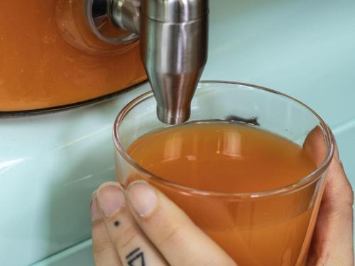 マコンにあるHôtel Mercure Mâcon Bord de Saôneのジューサーの横でお茶の入ったグラスを持つ手