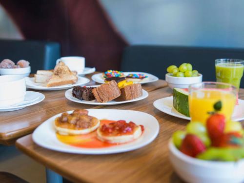 a wooden table topped with plates of food and fruit at Ibis Guaratingueta Aparecida - Circuito da Fé in Guaratinguetá