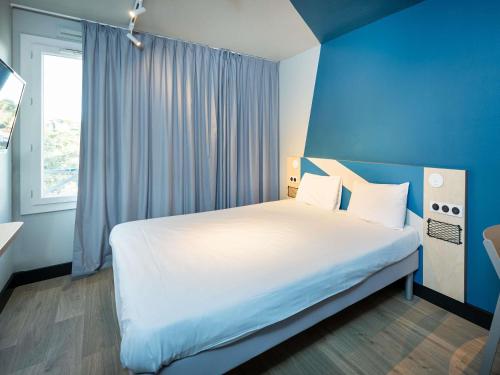 a bedroom with a large white bed with a blue wall at Ibis Budget Lyon Caluire Cité Internationale in Caluire-et-Cuire