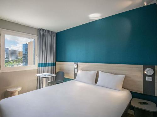 - une chambre avec un grand lit blanc et un mur bleu dans l'établissement ibis budget Nice Aeroport, à Nice