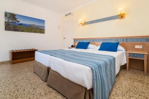a hotel room with a large bed with blue pillows at Globales Simar in Cala de Sant Vicenc