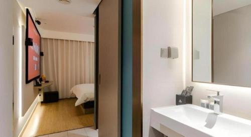 a bathroom with a sink and a mirror and a bedroom at Magnotel Ningbo Tianyi Plaza Railway Station in Ningbo