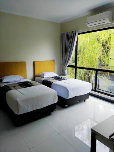 two beds in a room with a large window at Hotel Bima Majalengka in Majalengka