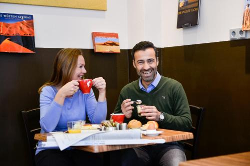 a man and woman sitting at a table drinking coffee at Hotel Sandmanns am Dom in Cologne