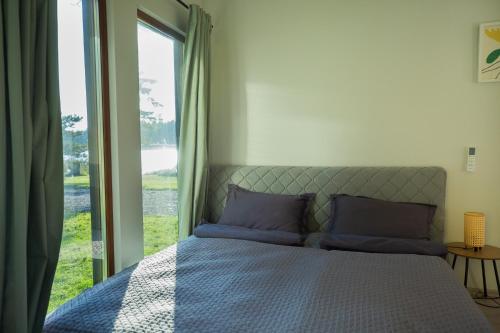 Cama con almohadas moradas en una habitación con ventana en RiverView Cozy Cabins in Jurmala with fishing opportunity, en Jūrmala