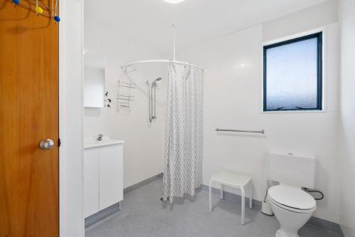 a white bathroom with a toilet and a window at Restful on Rutherford - Waikanae Holiday Home in Waikanae