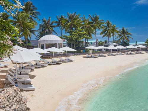 une plage avec des parasols et des chaises blanches et l'océan dans l'établissement Mövenpick Hotel Mactan Island Cebu, à Mactan