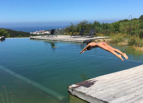 a man is jumping into a body of water at O Vale in Ericeira
