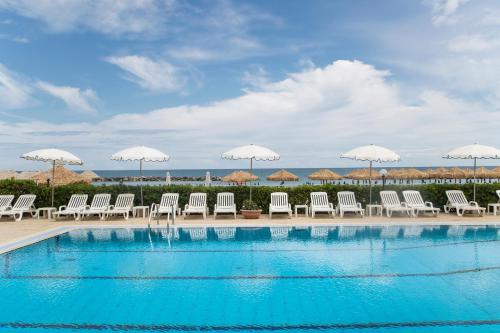 a swimming pool with white chairs and umbrellas at Hotel Mara in Ortona