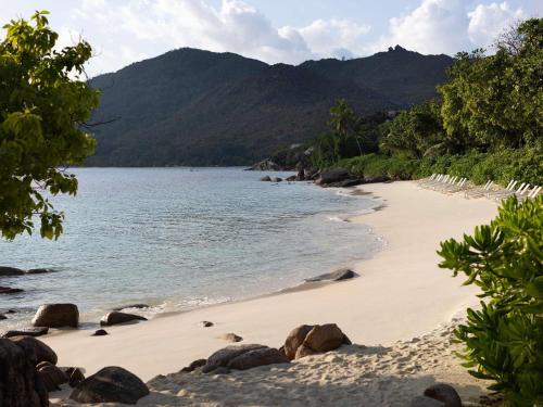 a beach with rocks and the water and mountains at Raffles Seychelles in Baie Sainte Anne