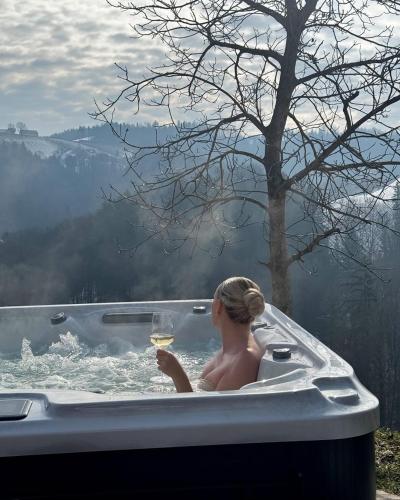 a woman in a bath tub with a glass of wine at Das KRANACH 28 Weinberg Hideaways mit Whirlpool und Sauna in Fötschach