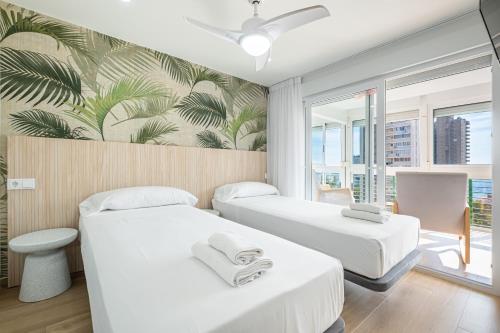 two beds in a room with a tropical wallpaper at Niza 11-A Apartment Levante Beach in Benidorm