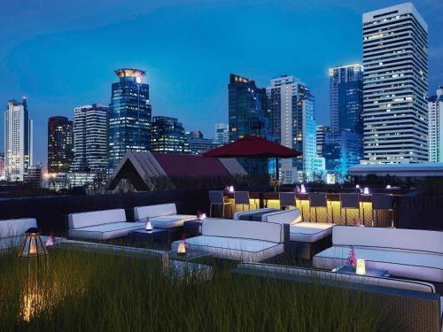 a rooftop bar with white couches and a city skyline at Mövenpick Hotel Sukhumvit 15 Bangkok in Bangkok
