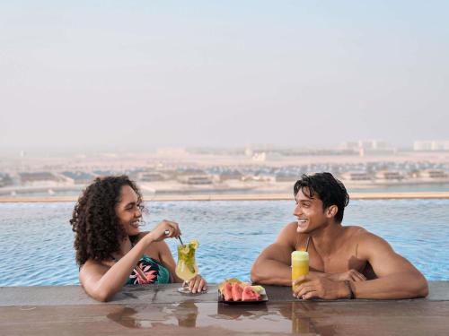 a man and woman sitting in the water with food and drinks at Aparthotel Adagio Dubai Deira in Dubai