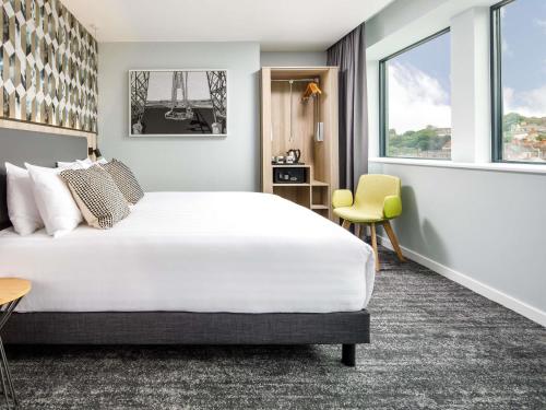 a hotel room with a large bed and a yellow chair at Mercure Newport in Newport