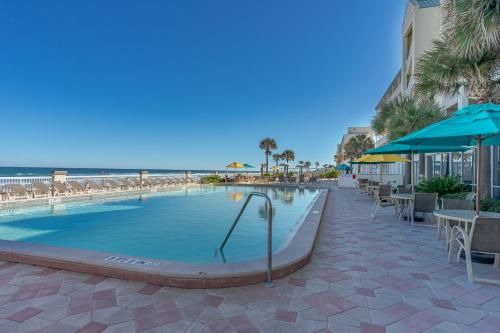 a swimming pool with tables and umbrellas next to the beach at Direct oceanfront, fantastic ocean view, separate bedroom ! - Pools open ! in Daytona Beach