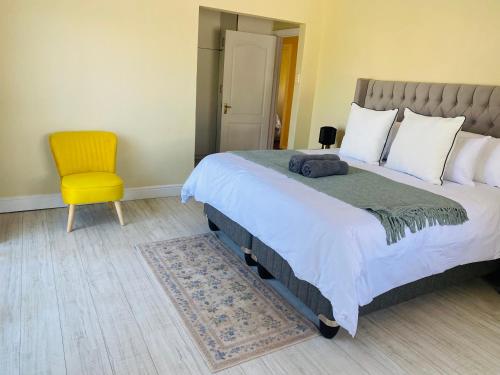 a bedroom with a large bed and a yellow chair at PJ Guest House in Gqeberha