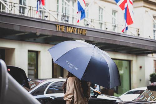 a person holding a blue umbrella in front of a building at The May Fair, A Radisson Collection Hotel, Mayfair London in London