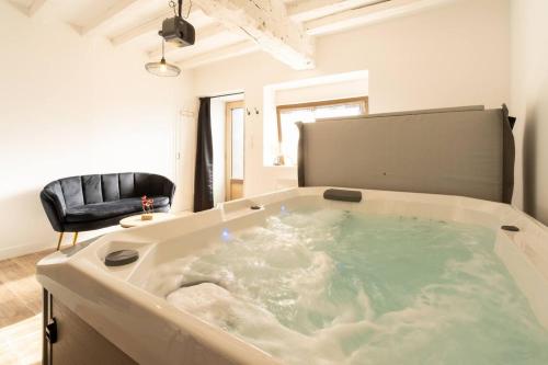 a large bath tub in a room with a chair at O Ricoul - Maison avec jacuzzi proche Rennes in Corps-Nuds