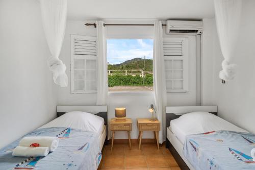 two beds in a room with a window at Appartement Aloé - Jardin et accès plage direct in Le Carbet