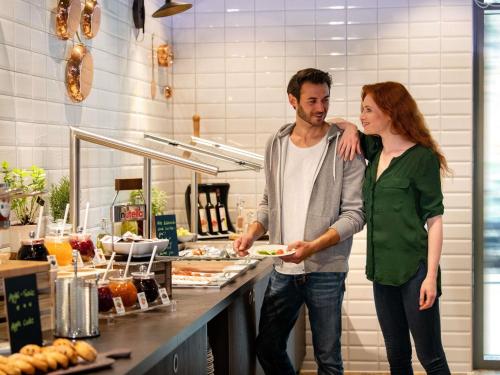 a man and a woman holding a plate in a kitchen at ibis Styles Hamburg Barmbek in Hamburg