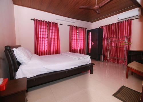 a bedroom with a bed with red curtains and a table at Edasseriathu Homestays Tiruvalla in Tiruvalla
