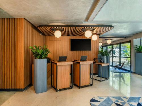 un hall d'entrée avec deux bureaux et une télévision au mur dans l'établissement Novotel SP Jardins, à São Paulo