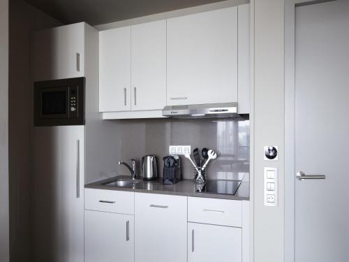 a white kitchen with a sink and a microwave at Aparthotel Adagio Paris Suresnes Longchamp in Suresnes