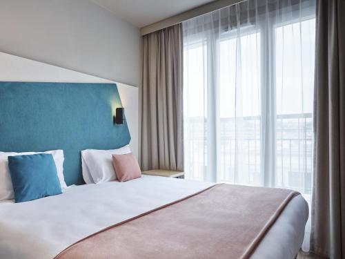um quarto com uma cama grande e uma janela grande em Aparthotel Adagio Paris Suresnes Longchamp em Suresnes