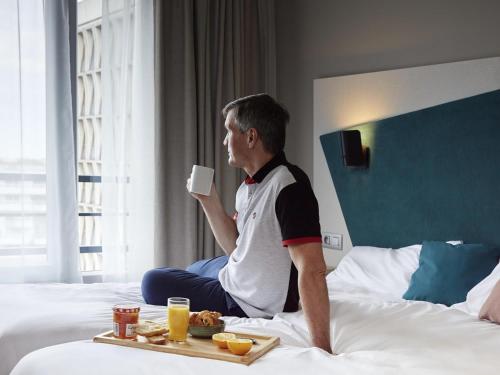 um homem sentado numa cama com uma bandeja de comida em Aparthotel Adagio Paris Suresnes Longchamp em Suresnes