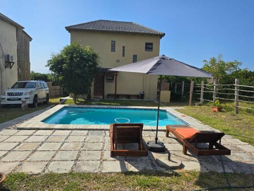 a pool with an umbrella and two chairs and a table at Casa Baleia Azul 8A Ponta Mamoli in Ponta Mamoli