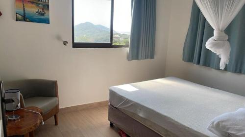 a bedroom with a bed and a chair and a window at Casa Baleia Azul 8A Ponta Mamoli in Ponta Mamoli