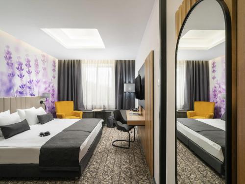 a hotel room with two beds and a mirror at Mercure Medias Binderbubi Hotel And Spa in Mediaş