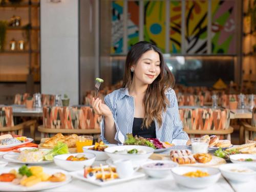パトゥムターニーにあるノボテルバンコクフューチャーパークランシットのテーブルに座って食事を食べている女性
