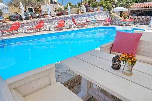 a bench next to a swimming pool with red chairs at Vasilaras Hotel in Skala